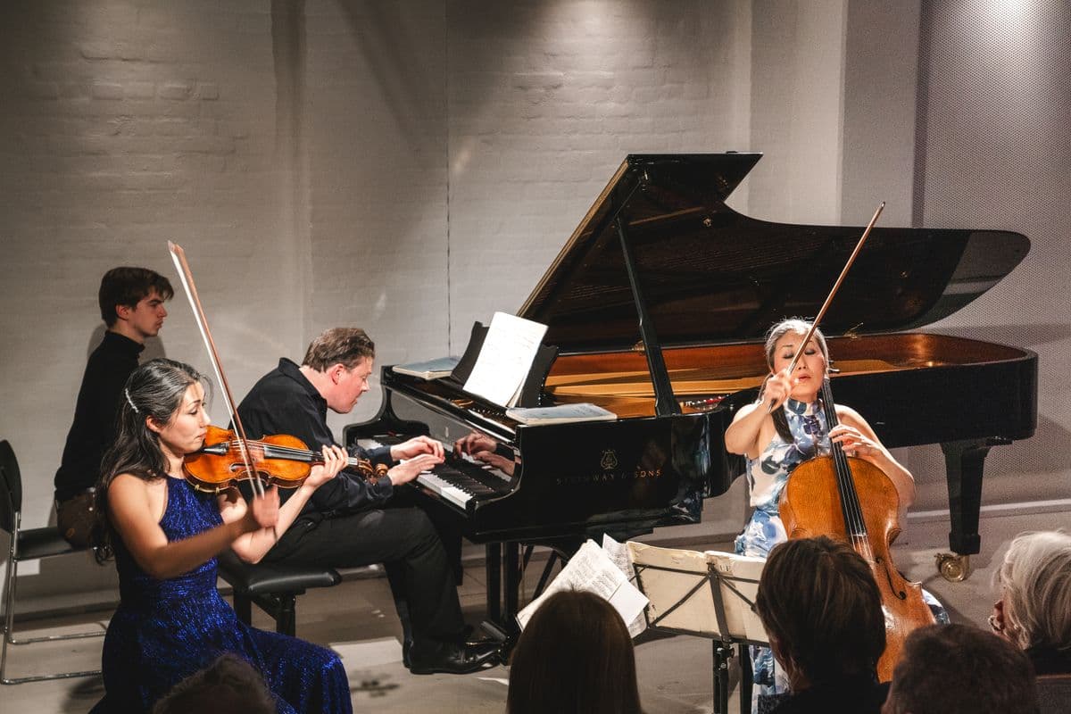 Billede af en koncert i Mogens Dahl Koncertsal, hvor en pianist, violinist og en cellist optræder. Koncerten viser de dygtige musikere i færd med at spille deres instrumenter, og fremhæver den musikalske kvalitet og atmosfære, der har været genstand for positive anmeldelser af koncertsalen og Mogens Dahl Kammerkor.